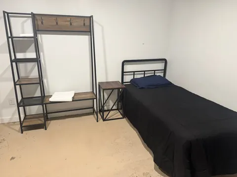 Furnished bedroom with a twin bed, nightstand and shelf-and-hook storage unit at the 2091 4th Ave E house