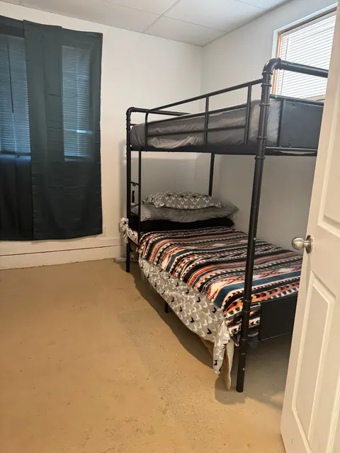 Bedroom with a metal bunk bed, blackout-curtained window and open door at the 2091 4th Ave E house