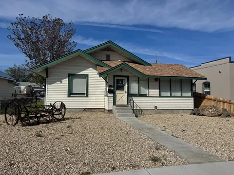 Front of the 212 4th Ave E house: cream siding with green trim, gravel yard, walkway and antique farm implement
