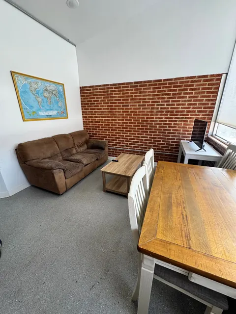 Common room at the 676 Shoup Ave W house with a brown sofa, world map, brick accent wall and dining table