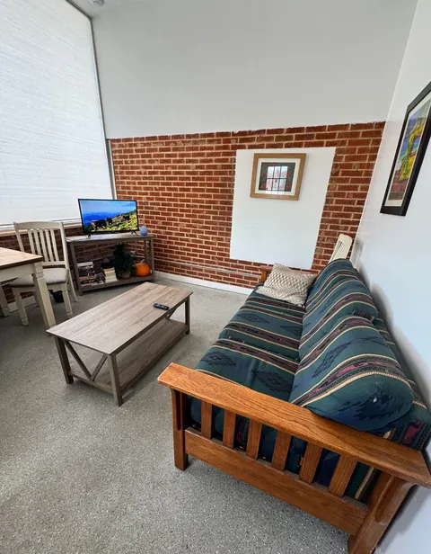 Common room at the 676 Shoup Ave W house with a wood futon, coffee table, TV console and brick accent wall