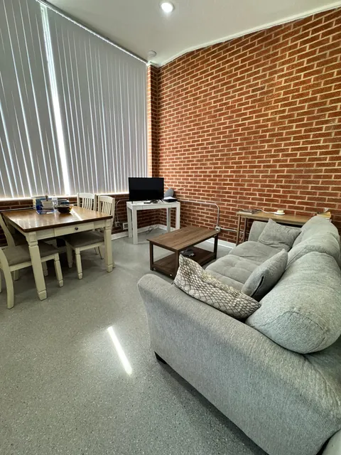 Common room at the 676 Shoup Ave W house with a gray sofa, coffee table and dining table by a brick wall