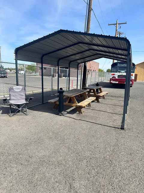 Covered outdoor area at the 676 Shoup Ave W house with two wooden picnic tables under a metal carport